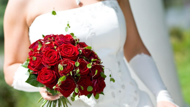 Ausschnitt Braut in weißem Kleid hält Strauß roter Rosen in Hand