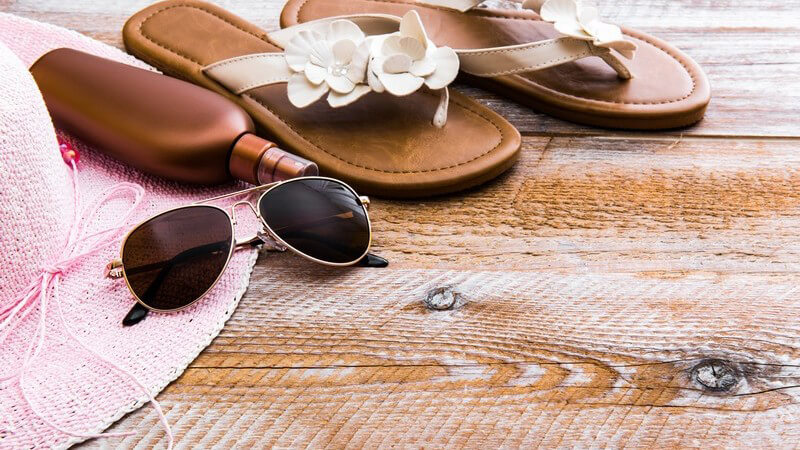 Sonnenhut, Sonnenbrille, Sonnencreme und Flip-Flops auf Holzuntergrund