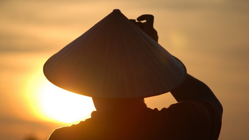 Mann mit vietnamesischem, spitzen Hut im Sonnenuntergang