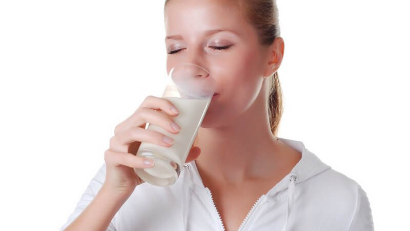 Junge Frau trinkt aus Glas mit Milch, weißer Hintergrund