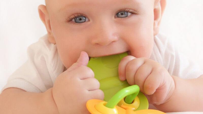 Lächelndes Baby kaut an Spielzeug rum