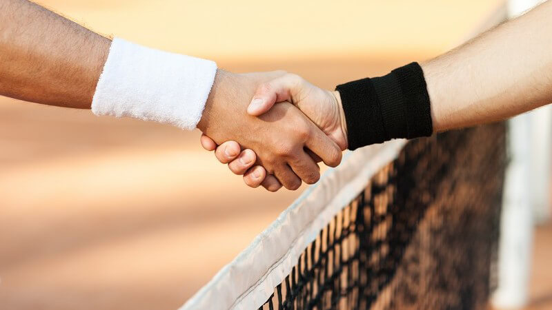 Tennisspieler mit weißem und mit schwarzem Schweißband am Handgelenk schütteln sich die Hände über dem Netz