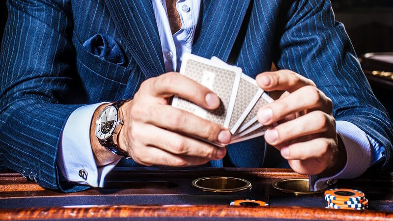 Mann in blauem Nadelstreifenanzug sitzt mit Karten und Chips an einem Casinotisch