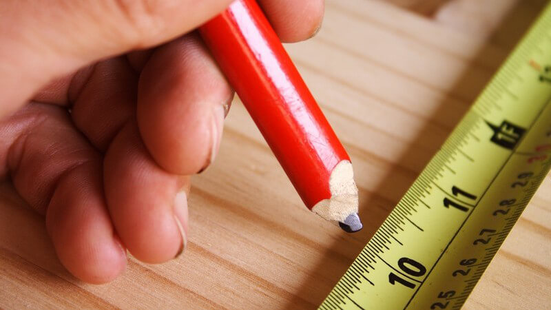 Bleistift wird auf Holzplatte neben Maßband gehalten
