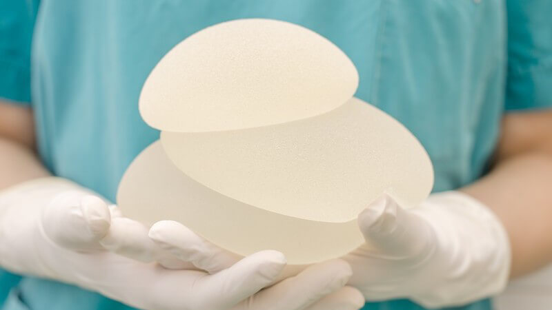 Chirurgin mit Schutzhandschuhen hält drei unterschiedlich große Brustimplantate in den Händen