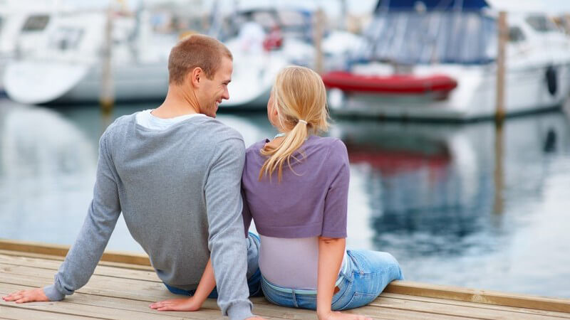 Junges Paar sitzt auf Steg am Hafen vor Booten