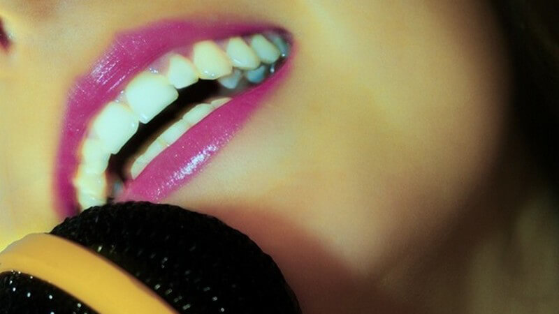 Rosa geschminkter Mund vor einem gelb umrahmten Mikrophon