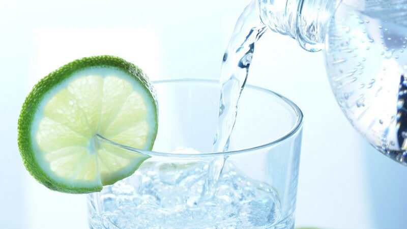 Mineralwasser wird aus Flasche in Glas geschüttet, Limettenscheibe an Glasrand