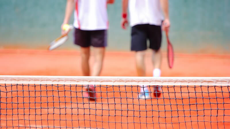 Netz eines Tennisplatzes, im Hintergrund zwei Tennisspieler