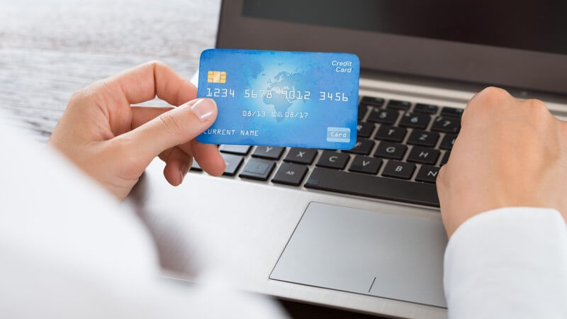 Geschäftsfrau hält eine blaue Kreditkarte und tippt die Daten in einen Laptop ein