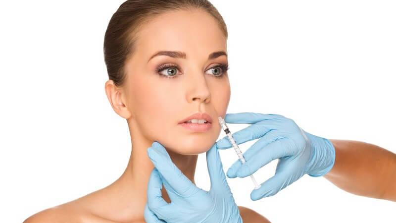 Hände in blauen Schutzhandschuhen spritzen einer Frau Botox in die Gesichtshaut, weißer Hintergrund