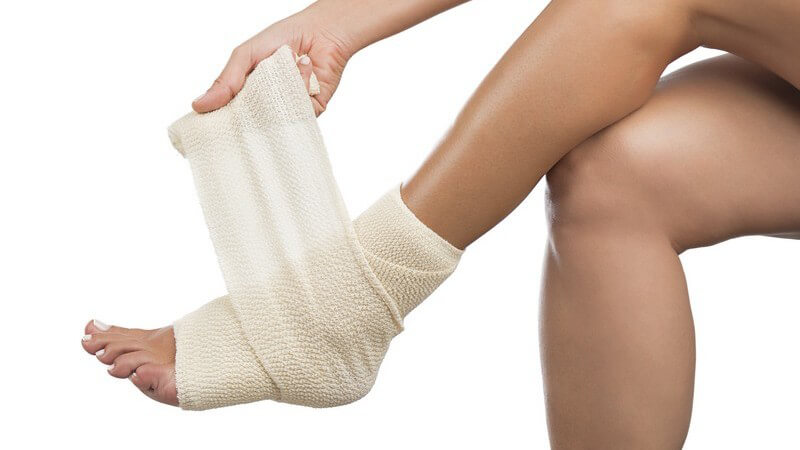 Frau bandagiert ihren Knöchel oder Sprunggelenk mit einer breiten Bandage