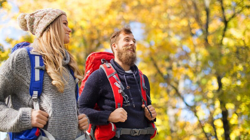 Junges Paar mit rotem und blauem Wanderrucksack beim Wandern im Herbst