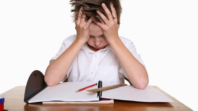 Junge hält verzweifelt Kopf in den Händen über Hausaufgaben