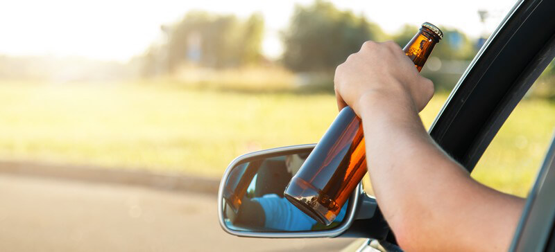 Autofahrer hält während der Fahrt eine Flasche Bier aus dem Fenster