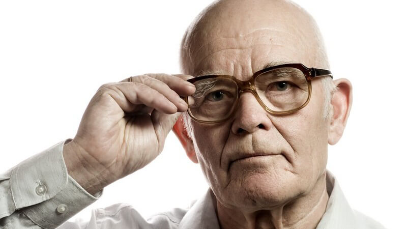 Alter Mann mit Glatze hält Hand an Brillenbügel, weißer Hintergrund