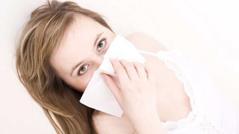 Junge dunkelblonde Frau mit Taschentuch putzt sich die Nase