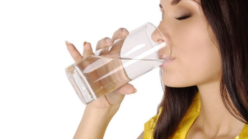 Junge Frau trinkt Wasser aus Glas, weißer Hintergrund