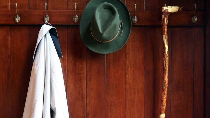 Jacke, Hut und Gehstock hängen an Haken in Garderobe