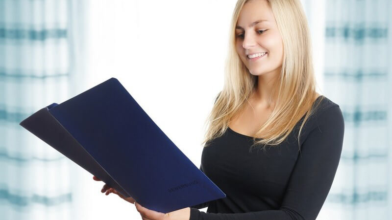 Junge Frau mit langen blonden Haaren beim Lesen in einer blauen Bewerbungsmappe