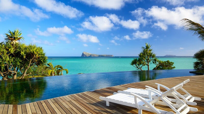 Mauritius: Blick von Holzterasse mit Liegestühlen und Infinity-Pool auf das türkise Meer, Sommerurlaub