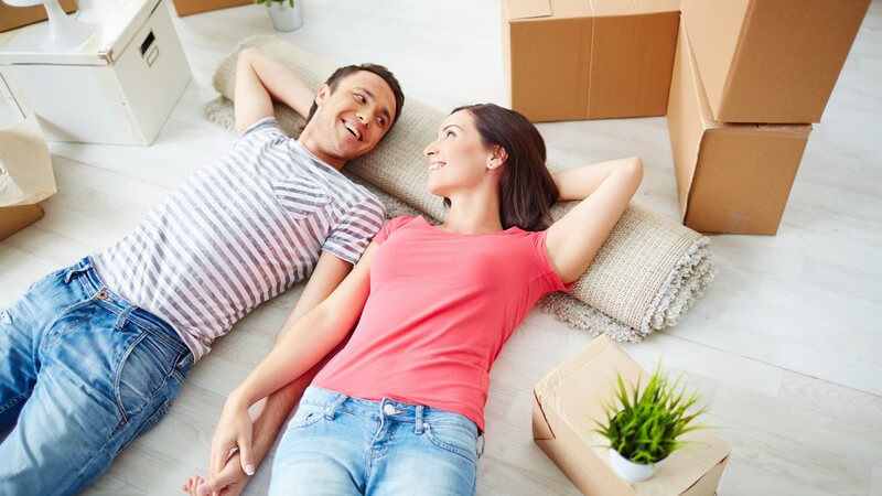 Zusammenziehen - Paar liegt in neuer Wohnung auf Fußboden neben Umzugskartons