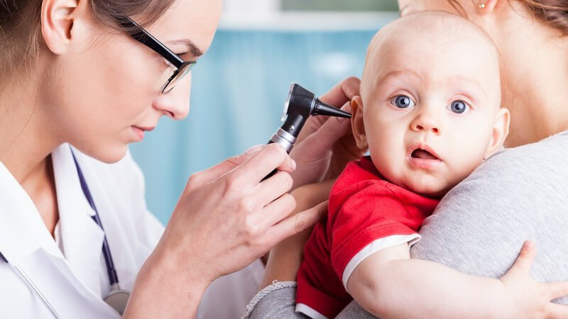 Kinderärztin untersucht ein Baby auf dem Arm seiner Mutter mit einem Otoskop im Ohr