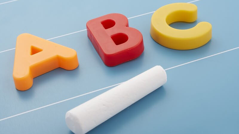 Buchstaben A B C aus Kunststoff liegen mit Kreide auf Tafel