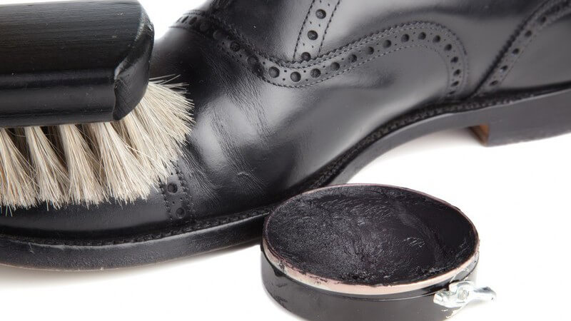 Lederschuh wird mit Bürste geputzt, daneben schwarzes Schuhfett