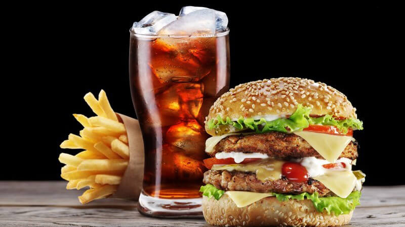 Pommes frites, Cola und Hamburger auf Holztisch vor schwarzem Hintergrund