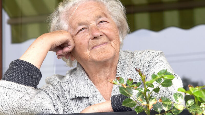 Nahaufnahme alte Frau mit weißen Haaren steht auf Balkon, Kopf auf die Hand gestützt