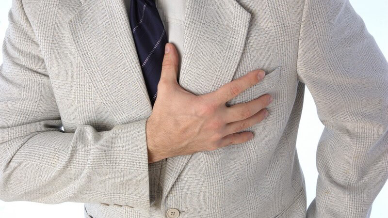 Mann im hellen Anzug und dunkelblauer Krawatte hat die rechte Hand auf den Brustkorb gelegt