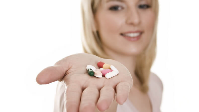 Blonde Frau hält ihre Hand mit bunten Tabletten in die Kamera