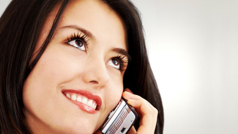 Dunkelhaarige, lächelnde Frau telefoniert mit Handy