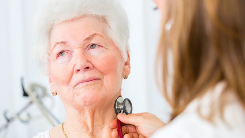 Ärztin hört eine Seniorin am Hals mit einem Stethoskop ab