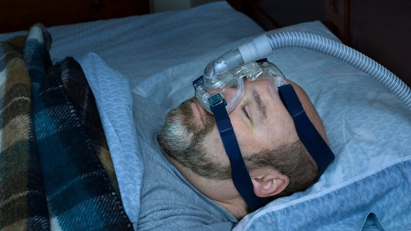 Schlafender Mann mit Beatmungsgerät für Schlafapnoe