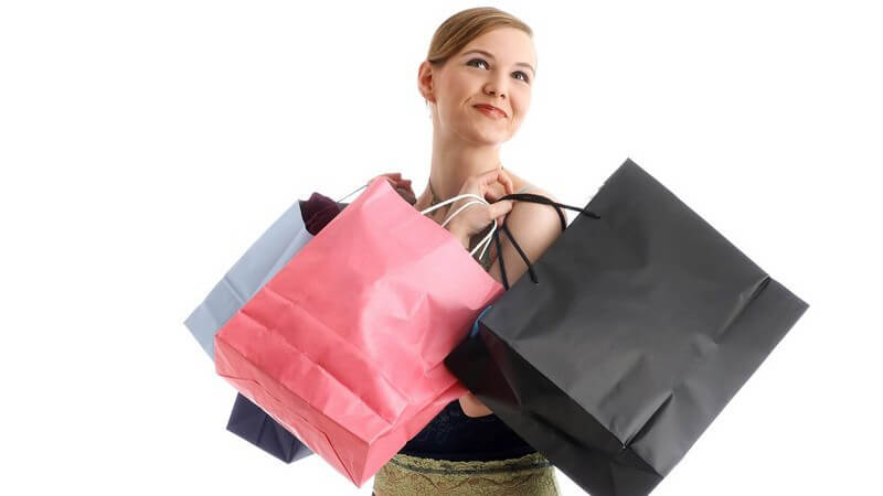 Junge Frau schaut glücklich nach oben, trägt vier Einkaufstaschen vom Einkaufen und Shoppen bei sich, weißer Hintergrund