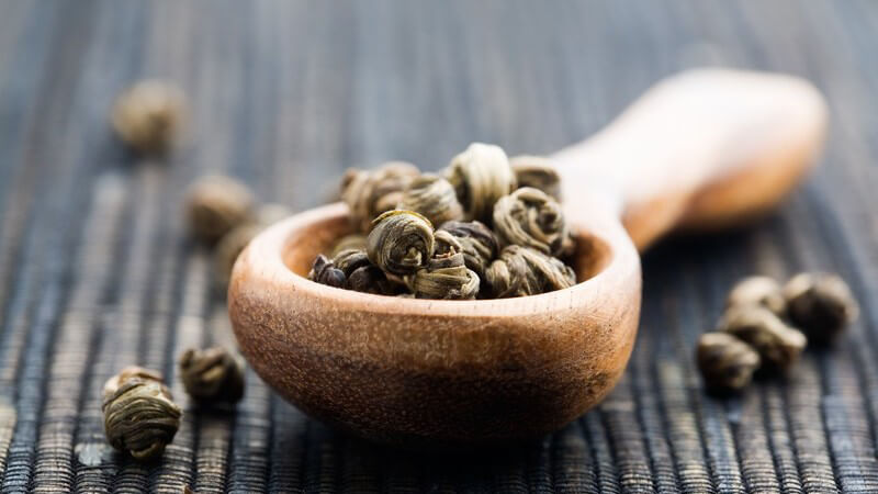 Nahaufnahme Grüner Tee, Blätter in kleinem Holzlöffel auf Bastmatte
