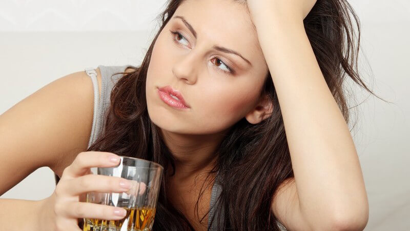 Unglückliche junge Frau hat Kopf auf Hand gestützt und hält Glas mit Alkohol