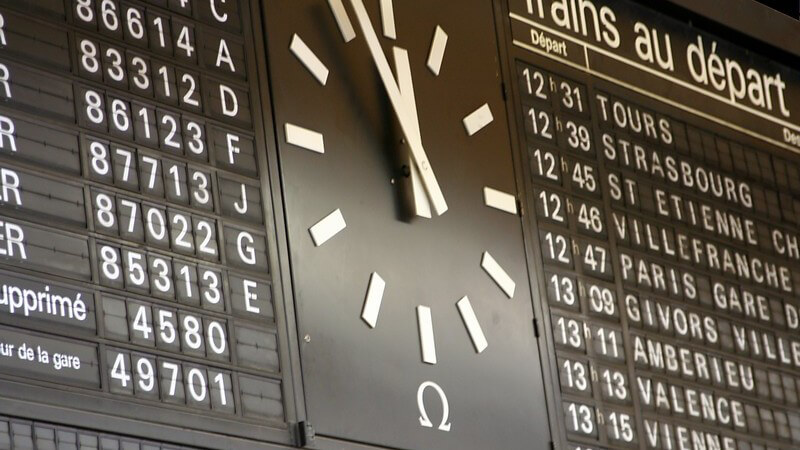 Abfahrtstafel mit Uhr am französischen Bahnhof, Uhrzeit kurz vor Zwölf