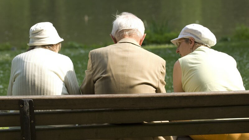 Rückansicht drei Senioren sitzen auf Bank im Park