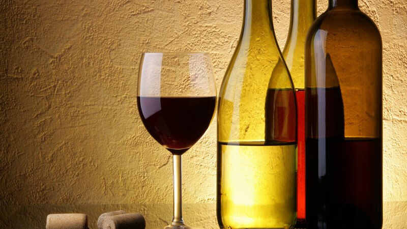 Drei Weinflaschen, daneben Glas mit Rotwein und Korken