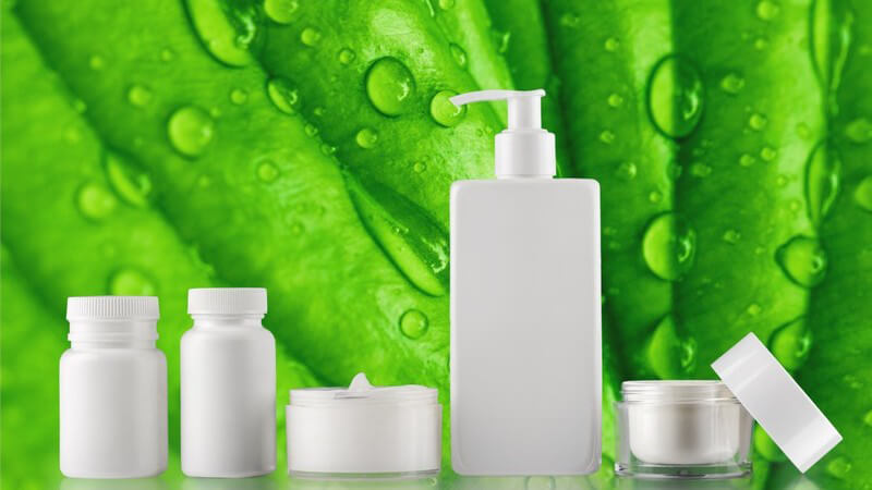 Fünf verschiedene weiße Kosmetikprodukte vor einem grünen Blatt voller Wassertropfen