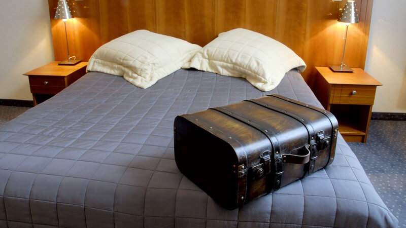 Schwerer Koffer auf einem Bett im Hotelzimmer