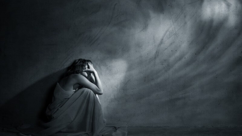 Schwarz-weiß Bild Frau hockt im dunklem leeren Zimmer an kahler Wand Depression Borderline Trauer