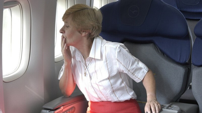 Reife Frau in weißer Bluse und rotem Rock auf Sitzplatz in Flugzeug, Fensterplatz, besorgter Blick