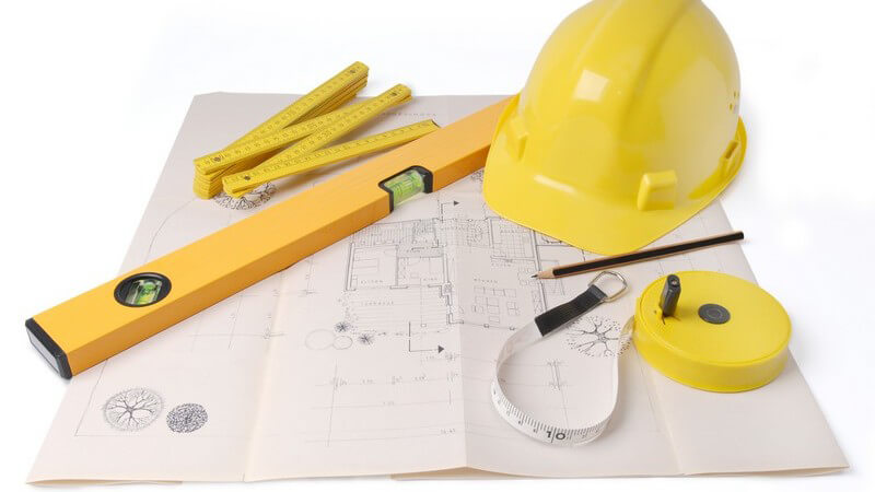 Bauarchitekt Utensilien wie gelber Hut, Zollstock, Wasserwaage, Maßband auf Bauplan