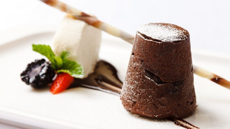 Schön garnierter Dessert-Teller mit einem Häufchen Schokoladenkuchen oder -pudding neben Vanilleeis und einer Stange