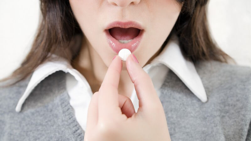 Frau führt Tablette in offenen Mund