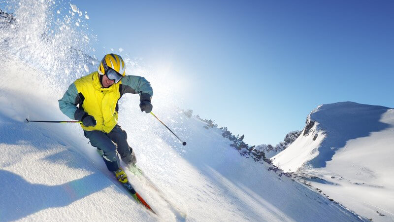 Skifahrer fährt steilen Hang in Bergen runter, blauer Himmel, Sonnenschein